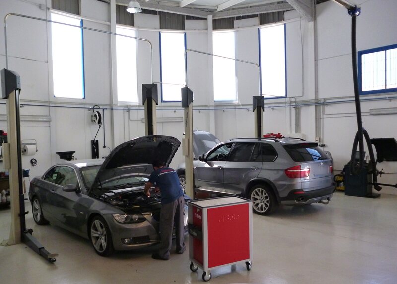 Un mecánico trabajando en un BMW Serie 3 en el taller, con un X5 al lado