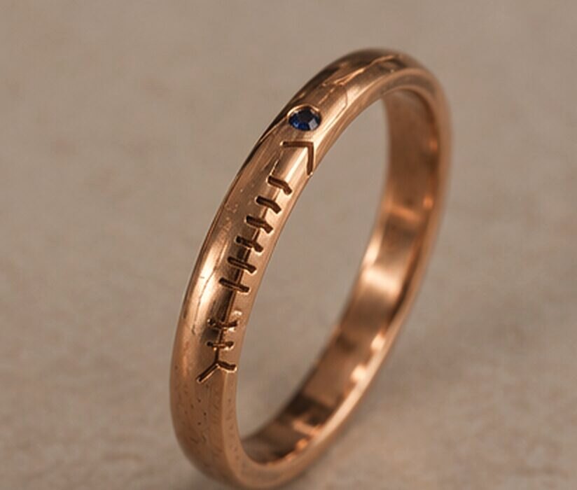 A thin rose gold band with a name cut in Ogham along the outside and a small sapphire set into the line