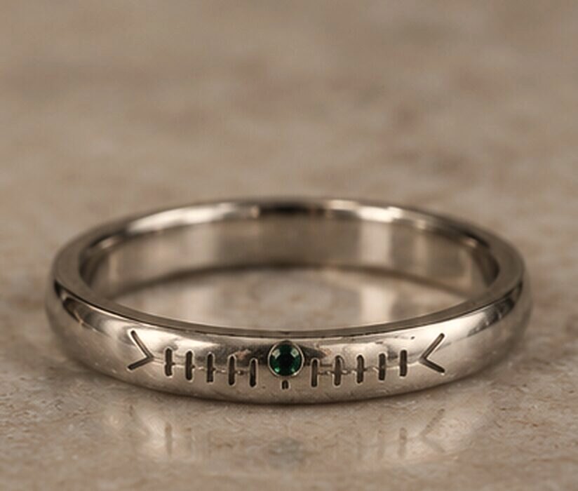 A medium white gold band with a name cut in Ogham along the outside and a small green tourmaline set into the line