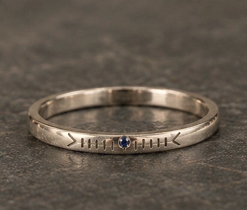 A very thin white gold band with a name cut in Ogham along the outside and a small sapphire set into the line