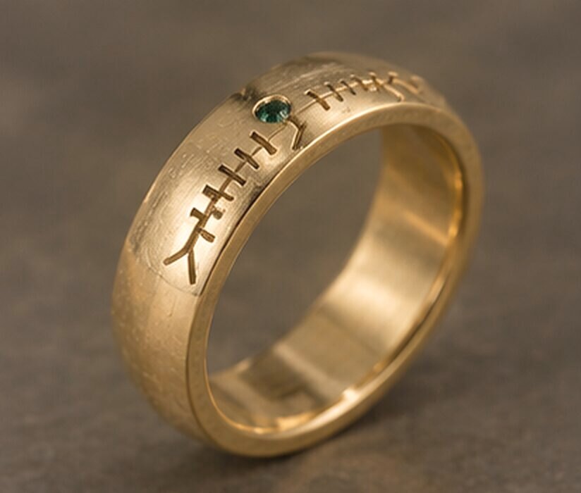 A thick yellow gold band with a name cut in Ogham along the outside and a small green tourmaline set into the line