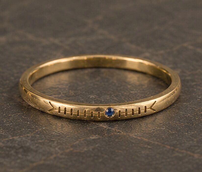 A very thin yellow gold band with a name cut in Ogham along the outside and a small sapphire set into the line