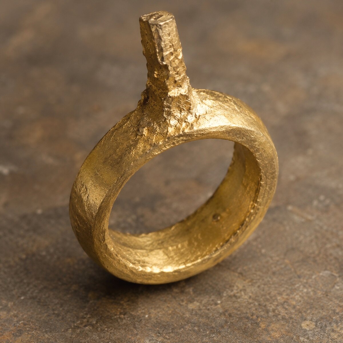 A rough, freshly cast gold ring with the sprue still standing up from the top of the band