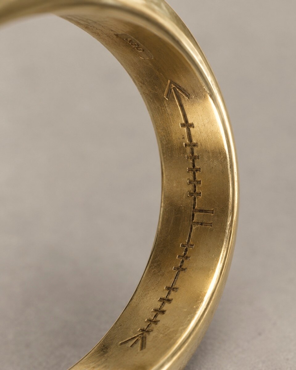 The inside of a gold band, with a name cut in Ogham along it: a line of short strokes between two arrow-like marks
