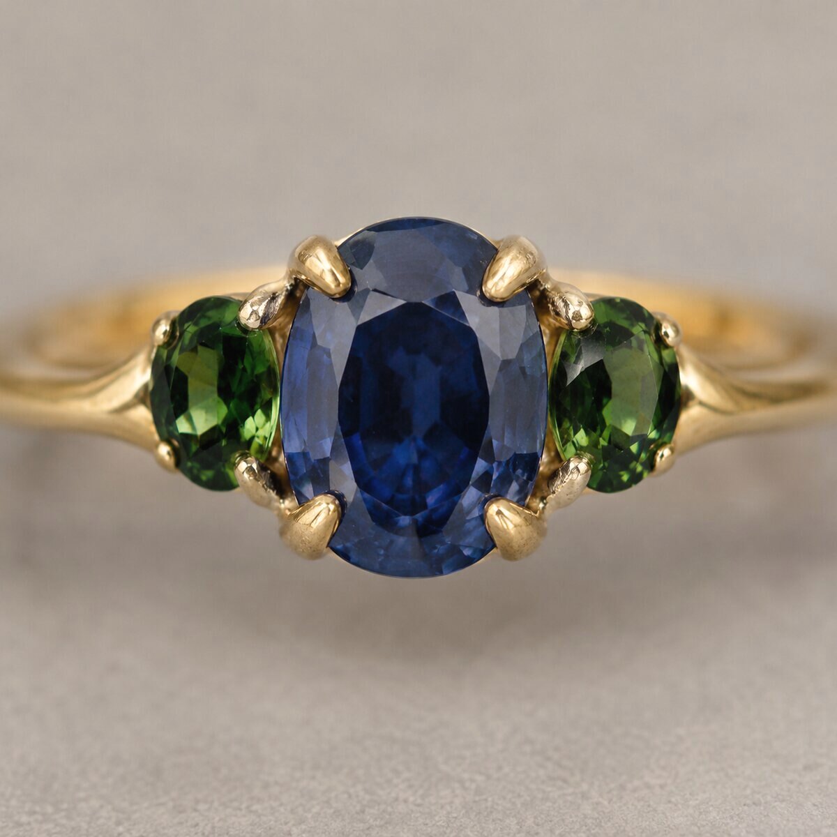 A gold ring with an oval blue sapphire held by four claws, and a small oval green tourmaline set either side