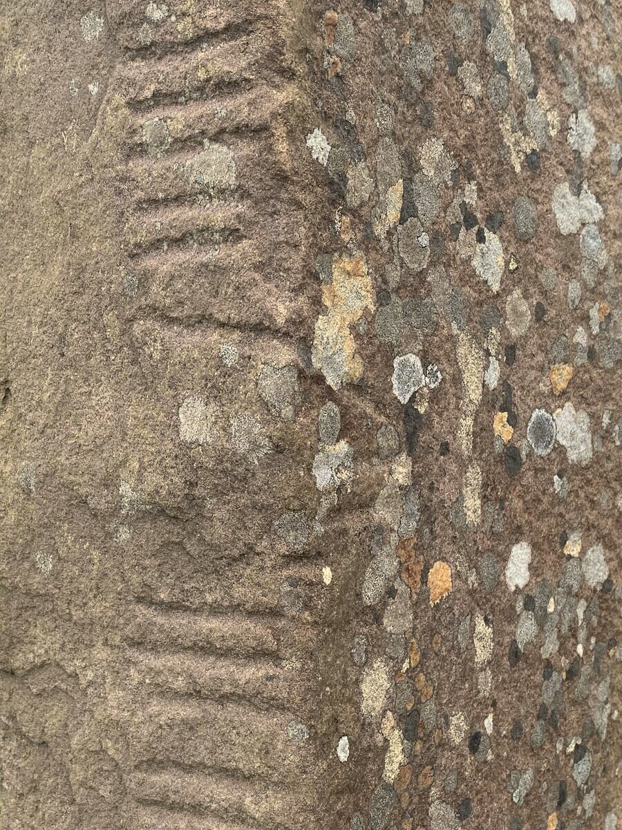 Close up of a lichen-spotted standing stone with two groups of short notches cut into its edge